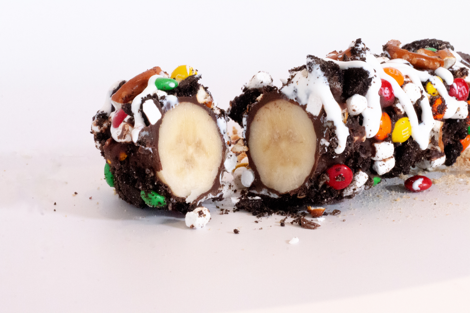Chocolate dipped banana covered with cookie crumbles, mini m&ms, and marshmallow drizzle