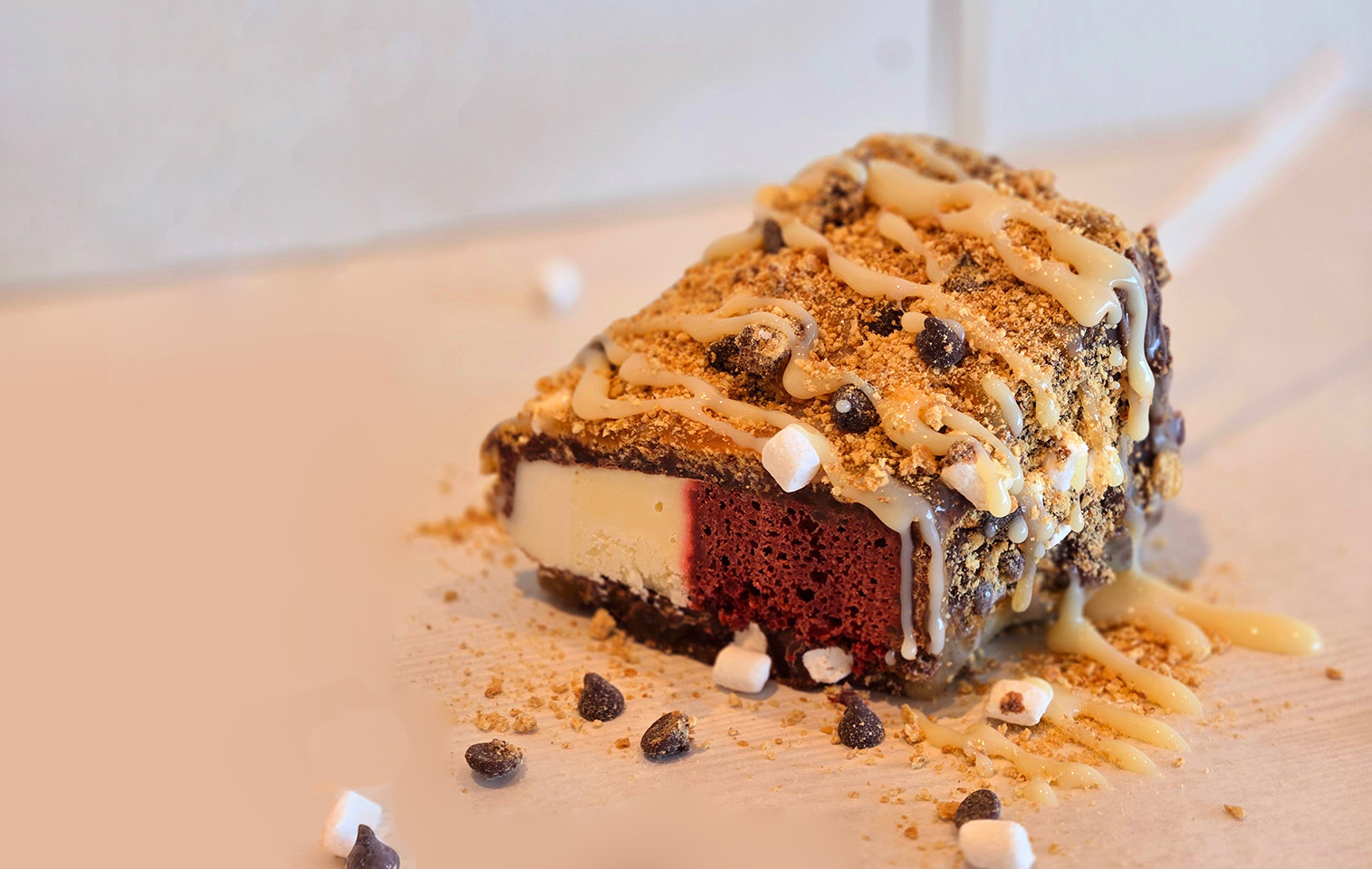 slice of red velvet cheesecake topped with s'mores topping and drizzled with sweetened condensed milk